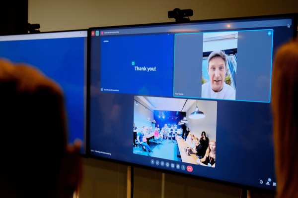 Successful hybrid meeting displayed on a screen, showing remote participants and an in-person group, with a “Thank you!” message on one part of the screen.