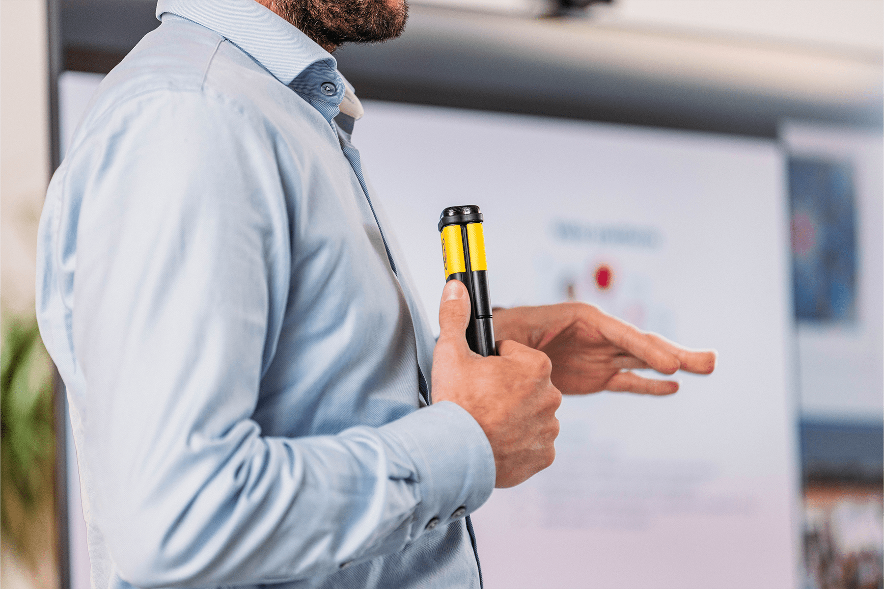 A close-up of a presenter holding a Catchbox Stick handheld microphone while gesturing during a presentation. The audio is being recorded for later use.