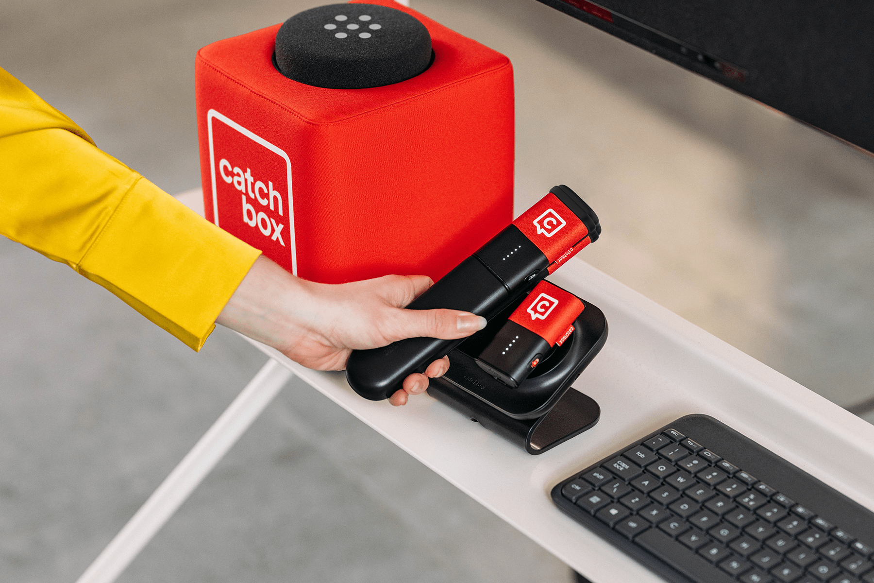 A person's hand reaching for a Catchbox Stick microphone, placed next to a Catchbox Cube and Clip microphone.