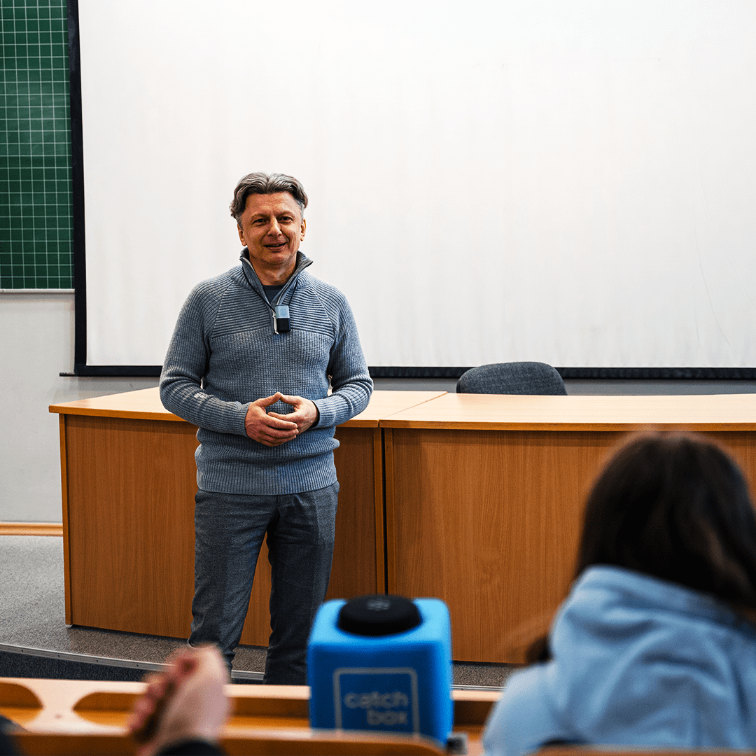 Professor standing in front of a student audience in a lecture theater, wearing a Catchbox Clip microphone.