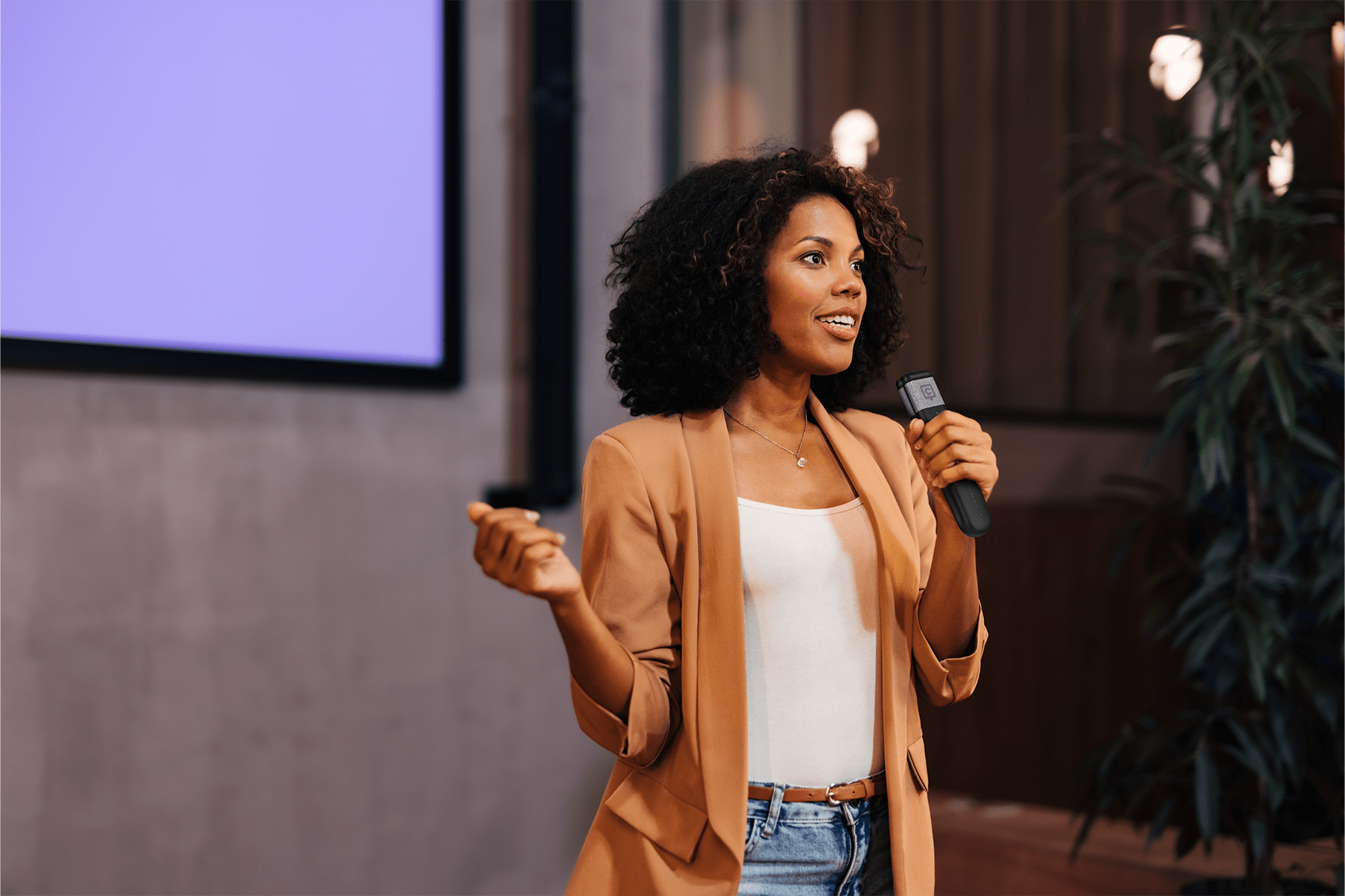 A woman presenting while holding a Catchbox handheld microphone, confidently speaking in front of a screen during an event