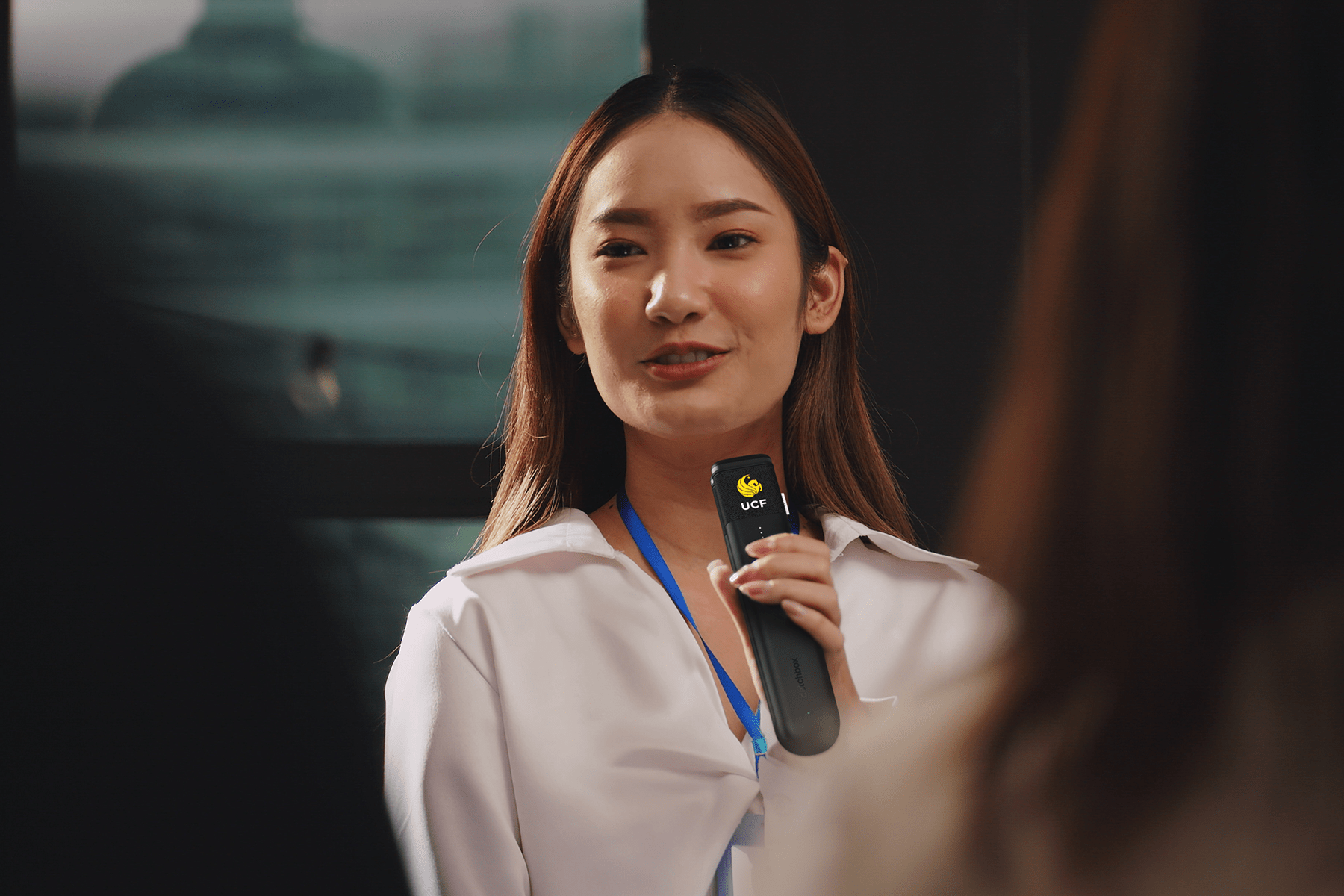 A woman speaking into a customized Catchbox handheld microphone with the UCF logo, engaging with an audience during a presentation.