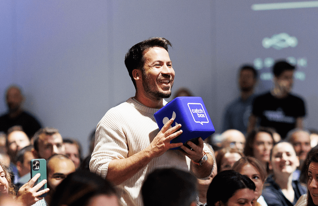 A conference attendee in the audience uses a Catchbox Cube microphone to ask a question to the presenter.